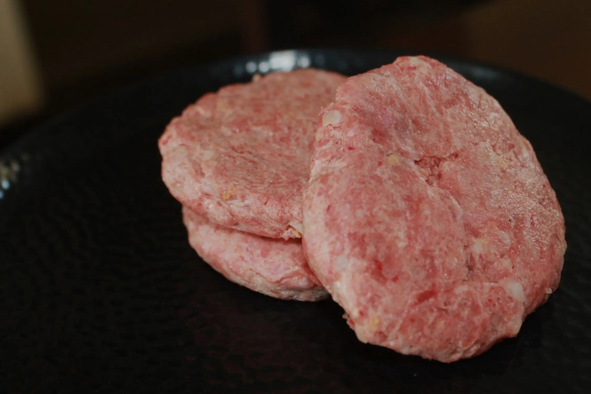 Three raw ground meat patties are stacked on a dark plate—ideal for those seeking premium Raw Cat Food - Duck and quail, inspired by www.barfindia.com's natural feeding philosophy.