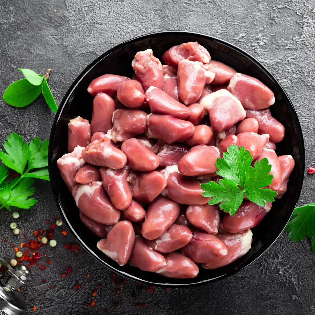 A black bowl of Dehydrated Chicken Hearts - 60gms from www.barfindia.com is garnished with parsley and sits on a dark textured surface, surrounded by scattered herbs and spices.