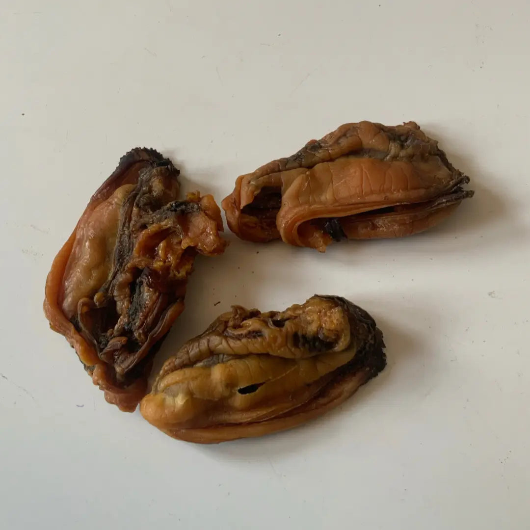 Three dehydrated green lipped mussels from www.barfindia.com’s Joint Health - Dehydrated Green Lipped Mussels (60 gms) are arranged on a white surface, with a shiny, wrinkled texture and dark edges, ideal for supporting your dog’s joint health.
