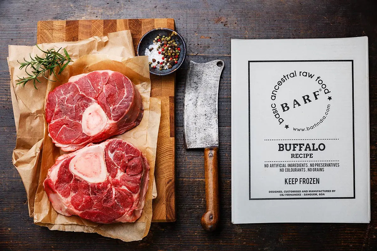 Two raw, pasture-raised buffalo meat steaks with bones lie on brown paper beside rosemary, peppercorns, a cleaver, and a www.barfindia.com Raw Dog Food - Buffalo Recipe 4 kgs pack—ideal for premium canine nutrition.